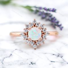 an opal and diamond ring sits on a marble surface next to lavender flowers,