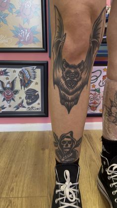 a person with tattoos on their legs standing in front of some framed pictures and paintings