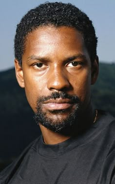 a close up of a person wearing a black t - shirt with mountains in the background