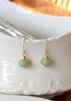 Using the same glass as the jade chrysalis, I've created a set of matching earrings. A refined, elegant companion to your Monarch chrysalis replica necklace in the same jade colored glass. Four 24k gold dots are perfectly placed on the bead. The findings are 14k gold-filled. I'm so happy to finally be offering these. Many people opt for the complex miniature chrysalis earrings, but it's lovely to be able to offer a simple, inexpensive option as well. Please note, if purchased with another piece, Elegant Light Green Earrings As Gift, Elegant Light Green Earrings For Gift, Elegant Green Glass Jewelry, Elegant Glass Earrings For Gift, Gold Hypoallergenic Jade Earrings, Hypoallergenic Gold Jade Earrings, Elegant Hypoallergenic Glass Earrings, Elegant Green Czech Glass Earrings, Jade Wire Wrapped Earrings For Gifts