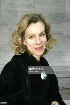 a woman with blonde hair smiling at the camera, wearing a black jacket and coat