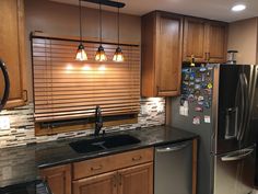 a kitchen with wooden cabinets and black counter tops, along with stainless steel refrigerator and dishwasher