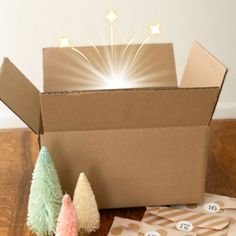 an open cardboard box sitting on top of a wooden table next to small christmas trees