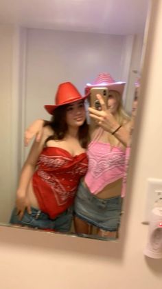 two women taking a selfie in a mirror with one wearing a red cowboy hat