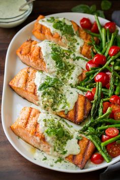 salmon and asparagus on a white plate topped with sour cream sauce next to cherry tomatoes