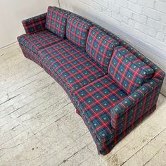 a blue and red plaid couch sitting on top of a wooden floor next to a white brick wall