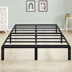 a black metal bed frame sitting on top of a wooden floor next to a white dresser