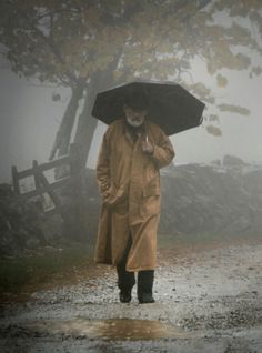 an old man walking in the rain with an umbrella