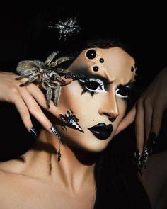 a woman with black and white makeup is holding her hands up to her face while wearing a spider costume