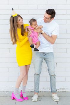 a man and woman holding a baby in front of a brick wall