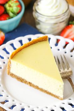 a slice of cheesecake on a white plate with strawberries and whipped cream in the background