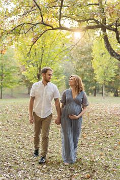 a pregnant couple walking through the leaves in an autumn park