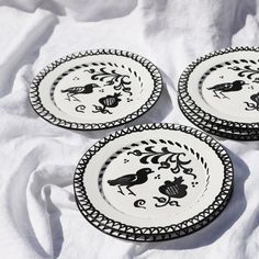 three black and white plates sitting on top of a white cloth covered tablecloth,