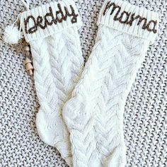 two white knitted mittens with the words daddy and mama written on them sitting on a gray blanket