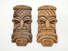 two carved wooden tiki heads on white wall with one facing the camera and another facing the viewer