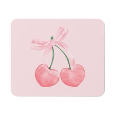 a pink mouse pad with two cherries and a bow on the end, against a light pink background