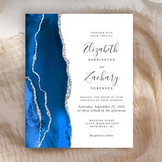 a blue and white wedding card with silver foil on the bottom, in front of a beige background