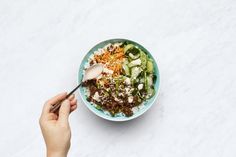 a person is holding a spoon over a bowl of food on a white tablecloth