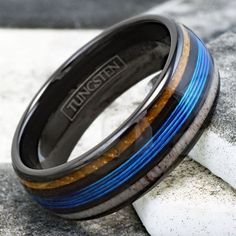 a black and blue ring with wood inlays on the inside is resting on some rocks