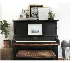 an old piano in a living room with plants and pictures on the wall above it