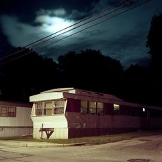 an old mobile home sitting on the side of a road at night with full moon in background