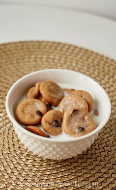 a bowl filled with cookies sitting on top of a woven place mat next to a cup of milk