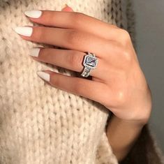 a woman's hand with white nails and a ring on her finger, wearing a sweater