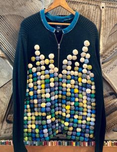 a blue sweater with multicolored beads hanging on a wooden hanger in front of a wall