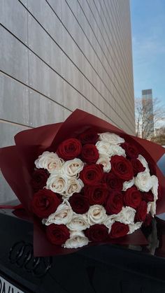 a bouquet of red and white roses sitting on the hood of a car in front of a building