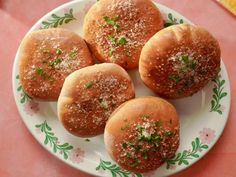 four small rolls on a plate with sprinkles and seasoning around them