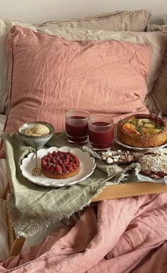 a tray with desserts and drinks on it sitting on a bed next to a pillow