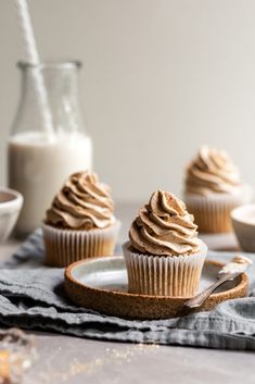 three cupcakes with frosting on a plate next to a glass of milk