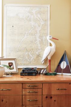 a white stork standing on top of a wooden dresser next to a map