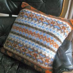 a black leather chair with a knitted pillow on it