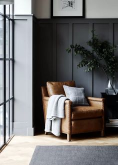 a living room with black paneling and leather furniture, including a brown chair in front of a window