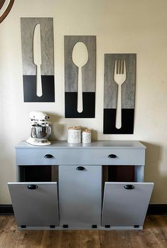 a white table topped with metal containers and utensils next to two paintings on the wall