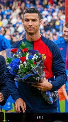 a man standing in front of a crowd holding a bouquet of flowers and wearing a red shirt