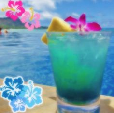 a blue and green drink sitting on top of a wooden table next to the ocean