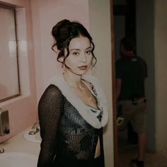 a woman standing in front of a bathroom mirror wearing a black dress and fur collar