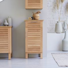 a wooden cabinet sitting next to a white vase and clock on a wall in a living room