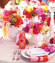 the table is set with white plates and goldware, pink napkins, and colorful flowers