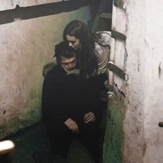 two people sitting on the ground in an old building, one is hugging the other