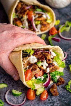 a hand holding a pita filled with meat and veggies on top of a table