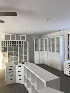 an empty room with white cabinets and drawers on the wall, in front of a ceiling fan