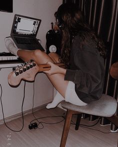 a woman sitting in front of a laptop computer on top of a wooden desk next to a guitar