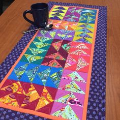 a table with a coffee cup on top of it next to a quilted table runner