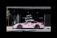 a pink sports car parked in front of a building with an anti social club sign on it's side