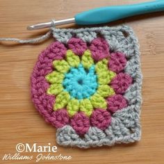 a crocheted square is sitting on a table next to a blue handled crochet hook