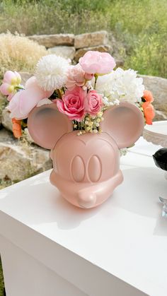 a vase with flowers in it sitting on top of a white table next to a rock wall