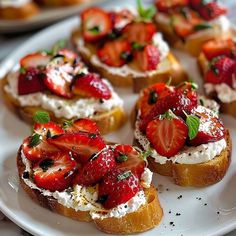 several pieces of bread with strawberries and cream cheese on them sitting on a white plate